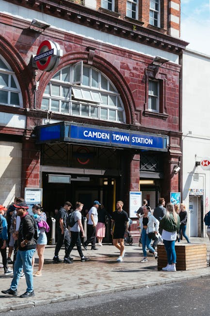 This image depicts the exterior entrance of Camden Town underground station, constructed with red brick and large arched windows that provide natural light to the interior. Above the entrance, there i
